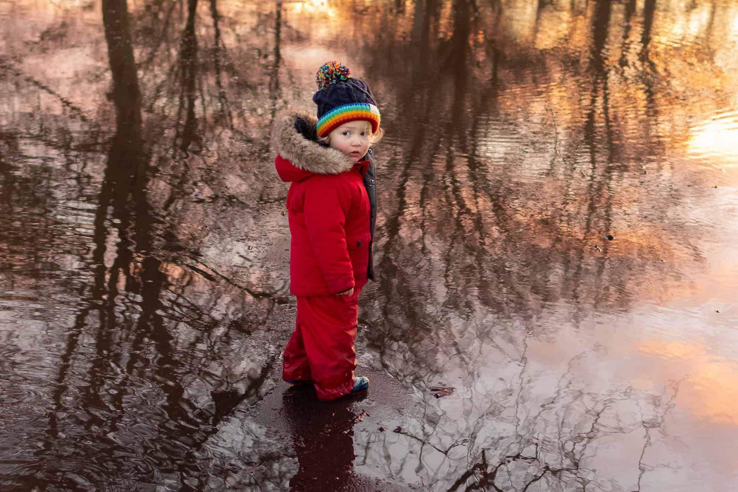 A boy stands in puddles in a flooded Higginson Park, the sunset reflected in the water.