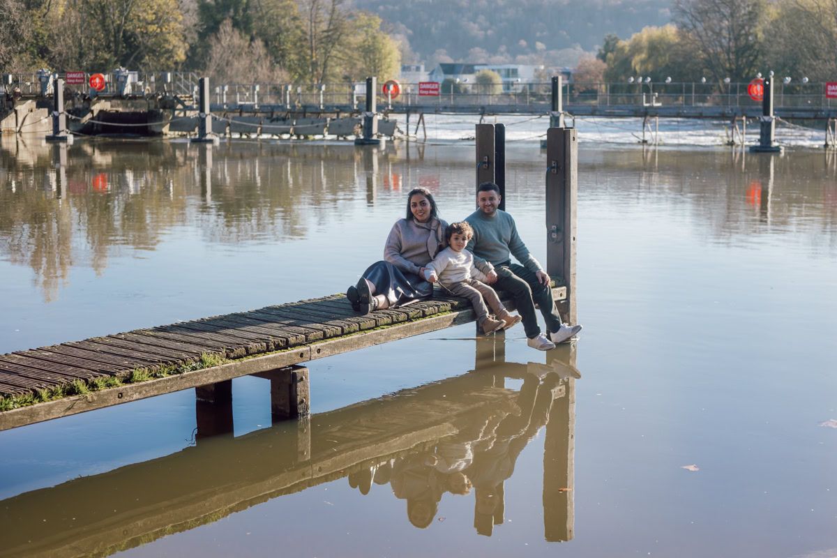 A family sit on the jetty on the river in Marlow during a family photosession.