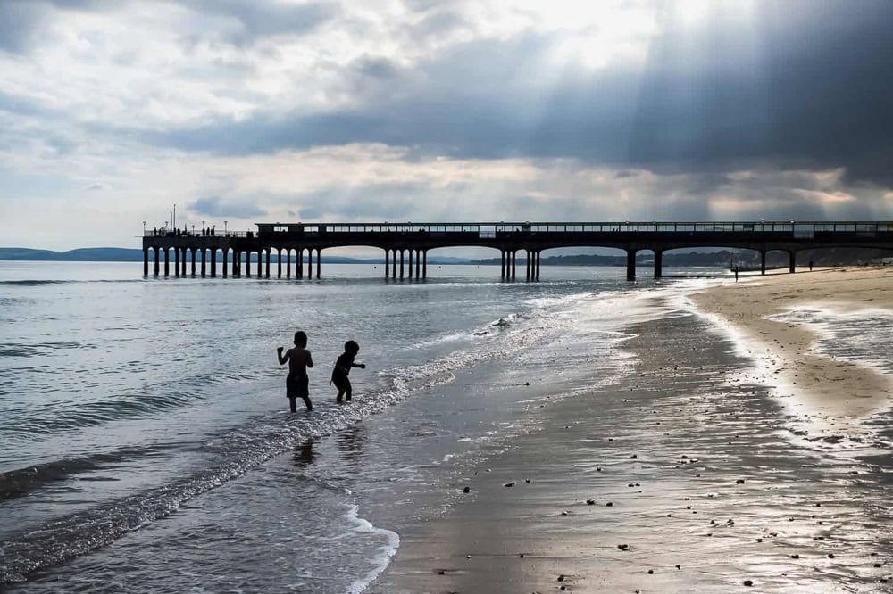 Two boys play in the surf under dramatic skies at Bournemouth Beach.