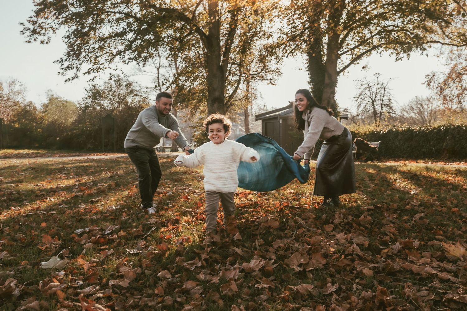 Two parents try to catch their young son with a blanket on an autumn photo session.