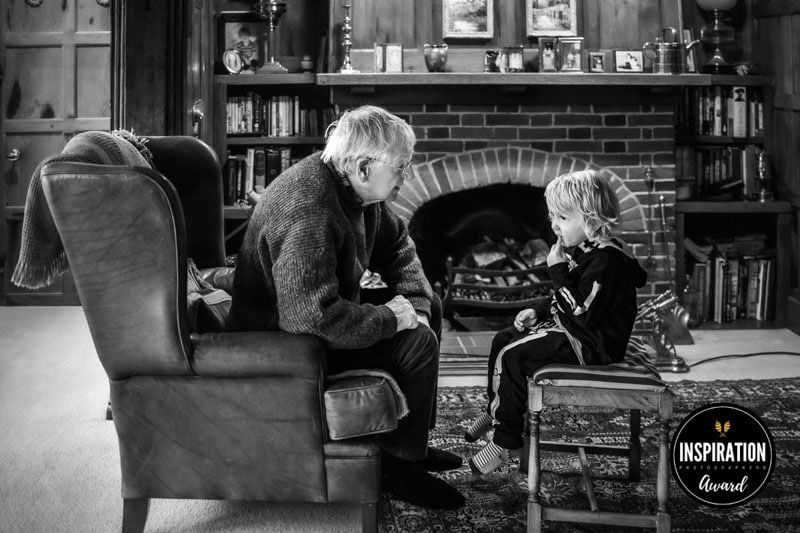 A grandfather chats to his grandchild in front of the fireplace in his sitting room.