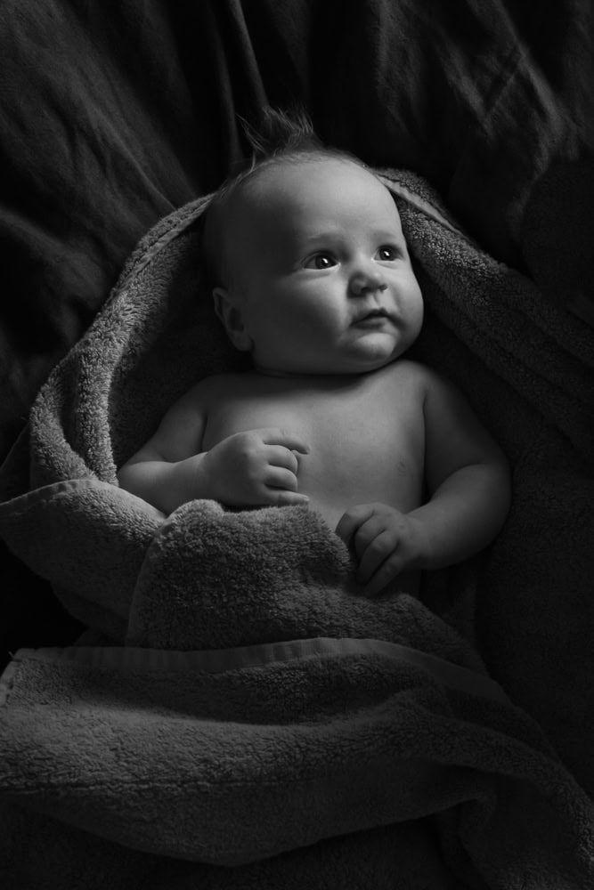 A 5 month old baby lies on his parent's bed wrapped in a a towel after a bath.