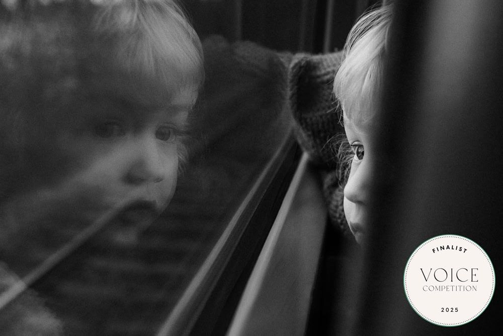 A young boy on a train, his reflection shown in the window.