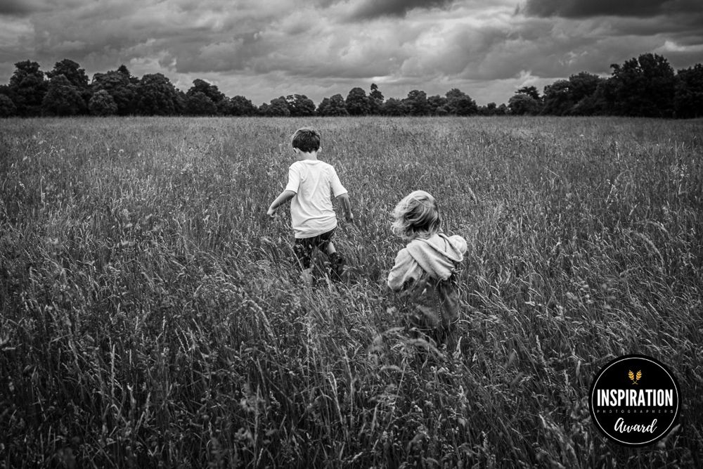 Two boys walk through a field of long grass on a windy overcast day.