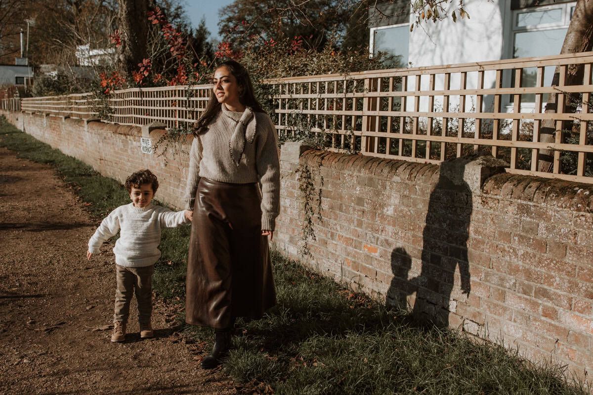 A mother and son hold hands walking from Marlow Bridge to Higginson Park, their shadows falling to the side.