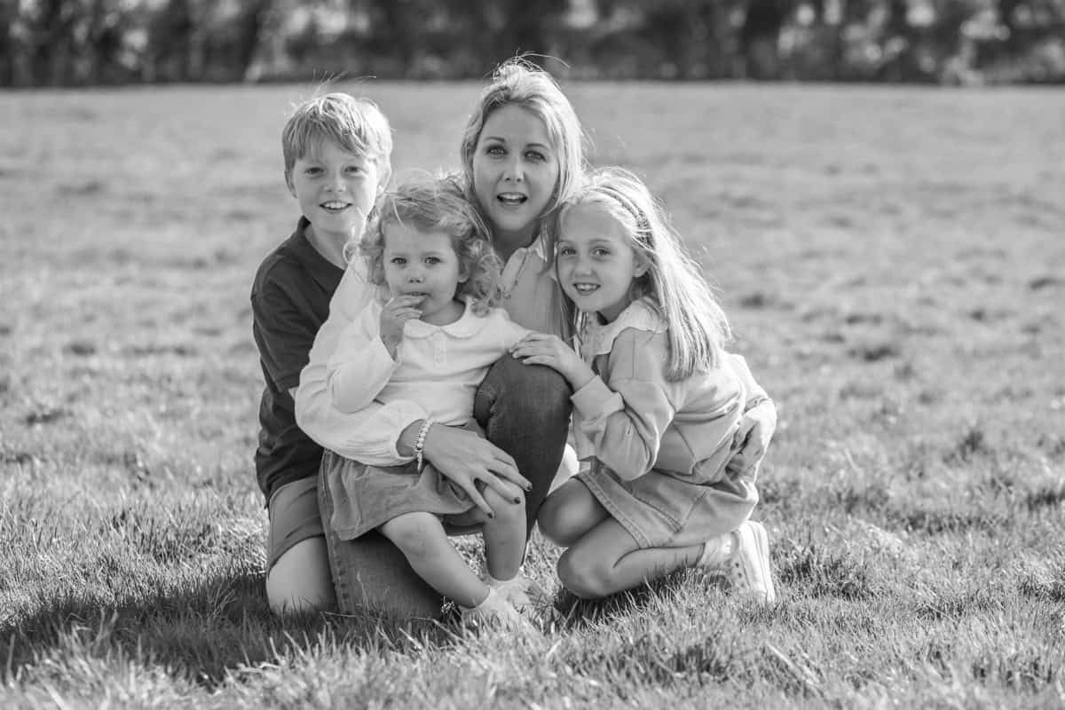 A mother hugs her three children in an outdoor location.