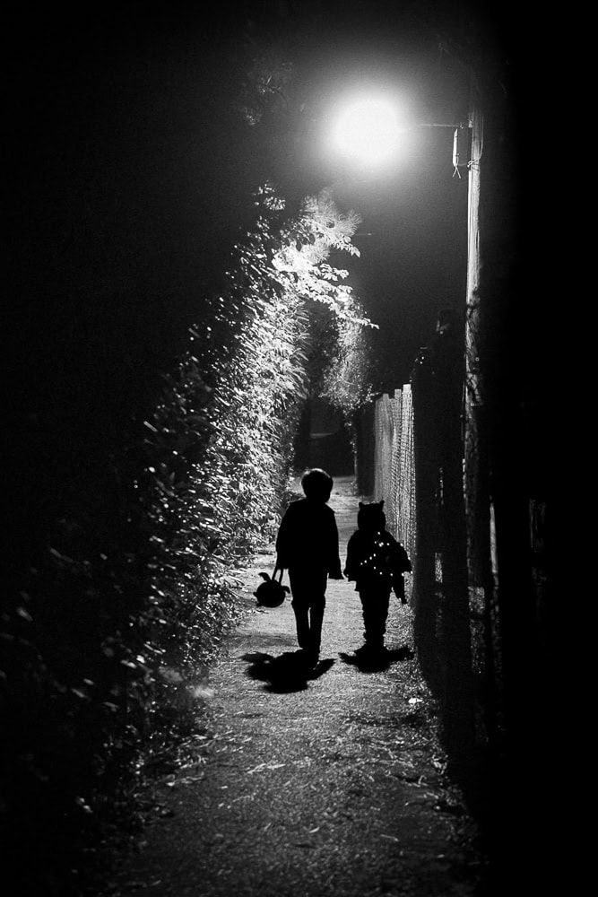 Two boys walk down a lane light by a single street light near Oak Tree Road in Marlow on halloween.  They carry trick or treat buckets.