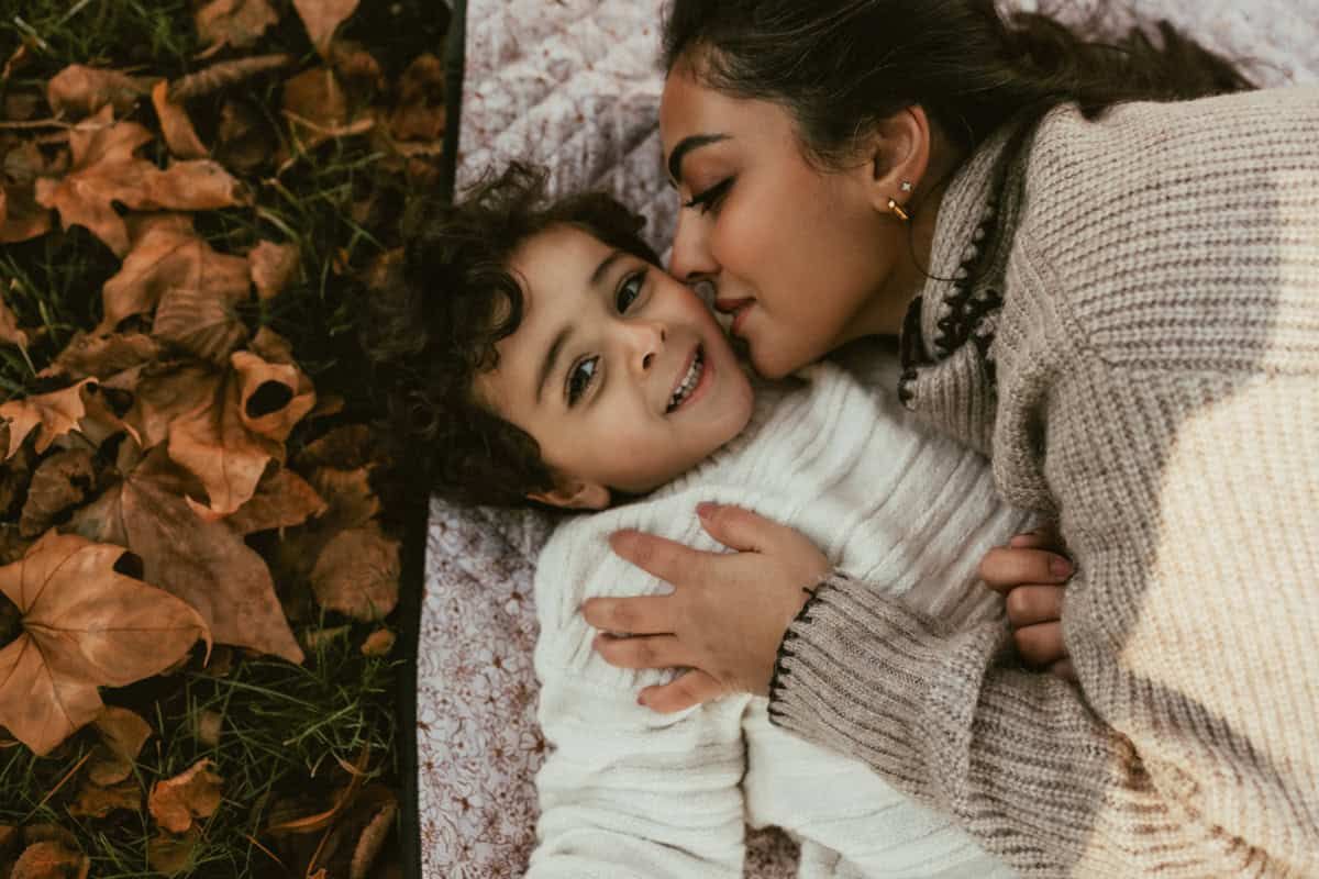 A mother kisses her son while they lie together on a picnic blanket.