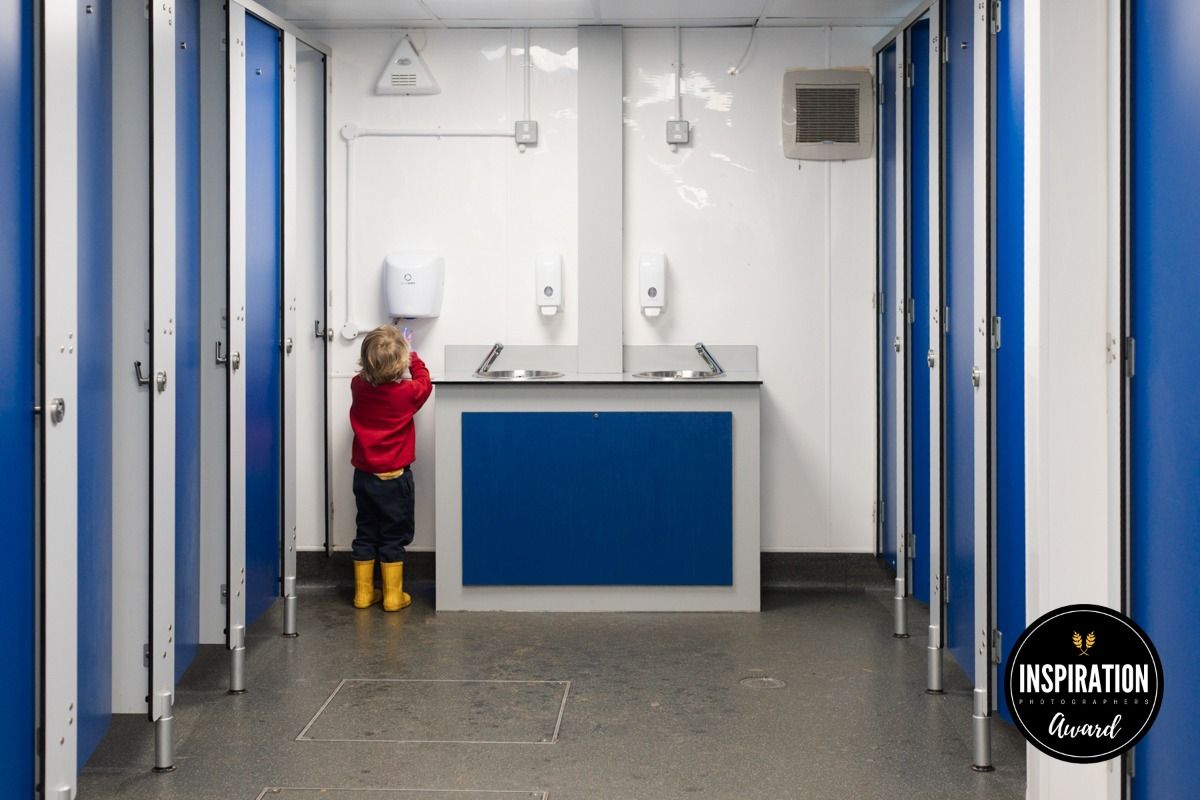 A young boy dries his hands in a public bathroom.  Red, yellow and blue are the only colours in the scene.
