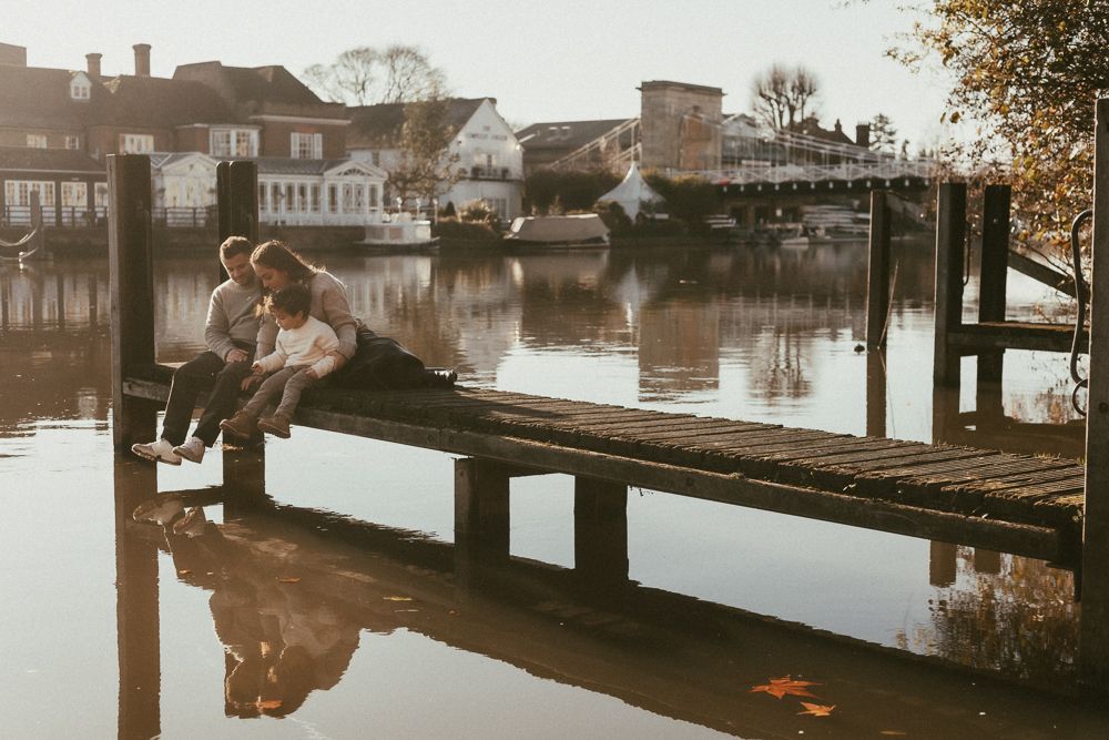A family of three sit on a jetty in the river opposite the Compleat Angler in Marlow.