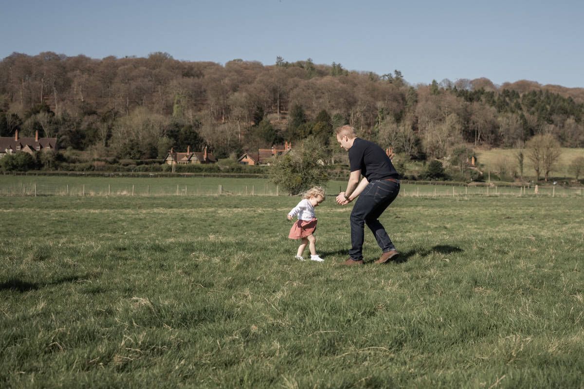 A father reaches out his arms to his young daughter, who is showing him her bad knee.