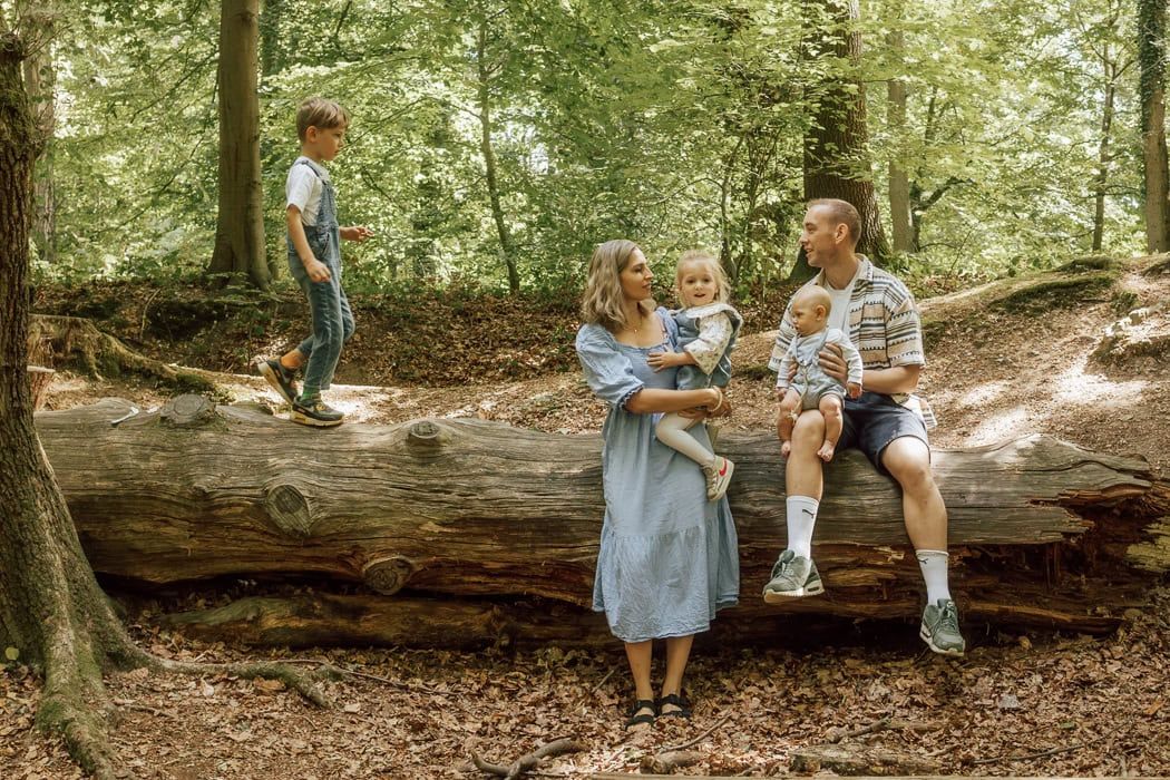 A family sit on a fallen tree in Marlow Common- their son walks across the tree towards them.