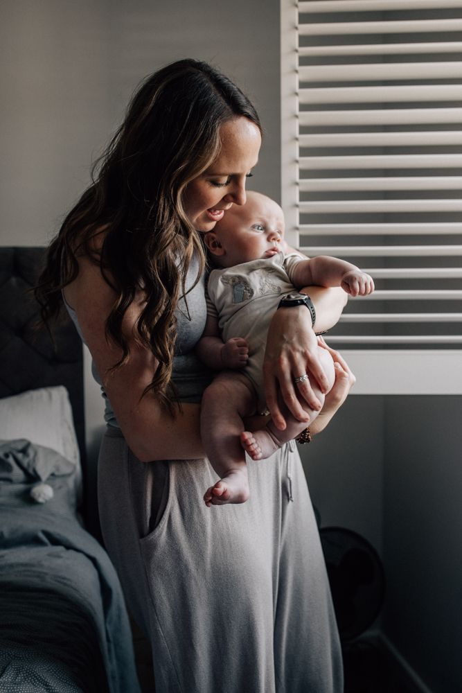 A mother holds her baby in front of a shuttered window.