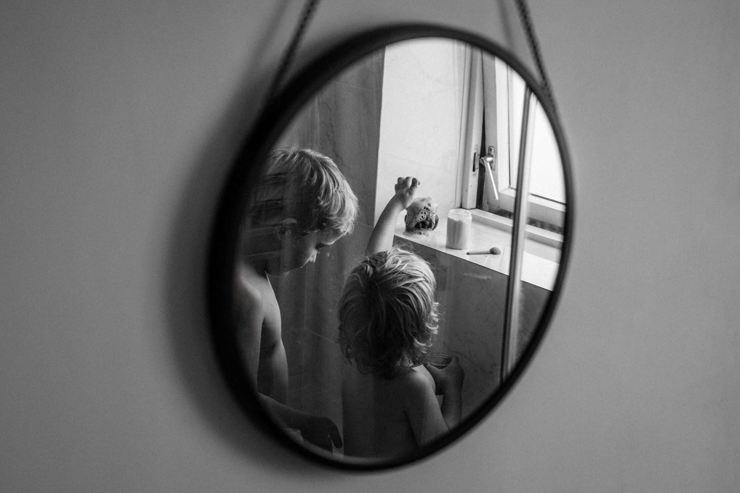 A round mirror reveals the reflection of two brothers playing at bathtime.  One is covered in Chickenpox spots.
