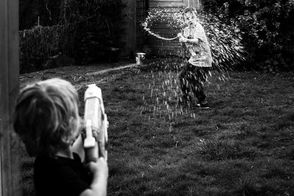 Two boys having a water gun fight in their garden near Marlow, UK.