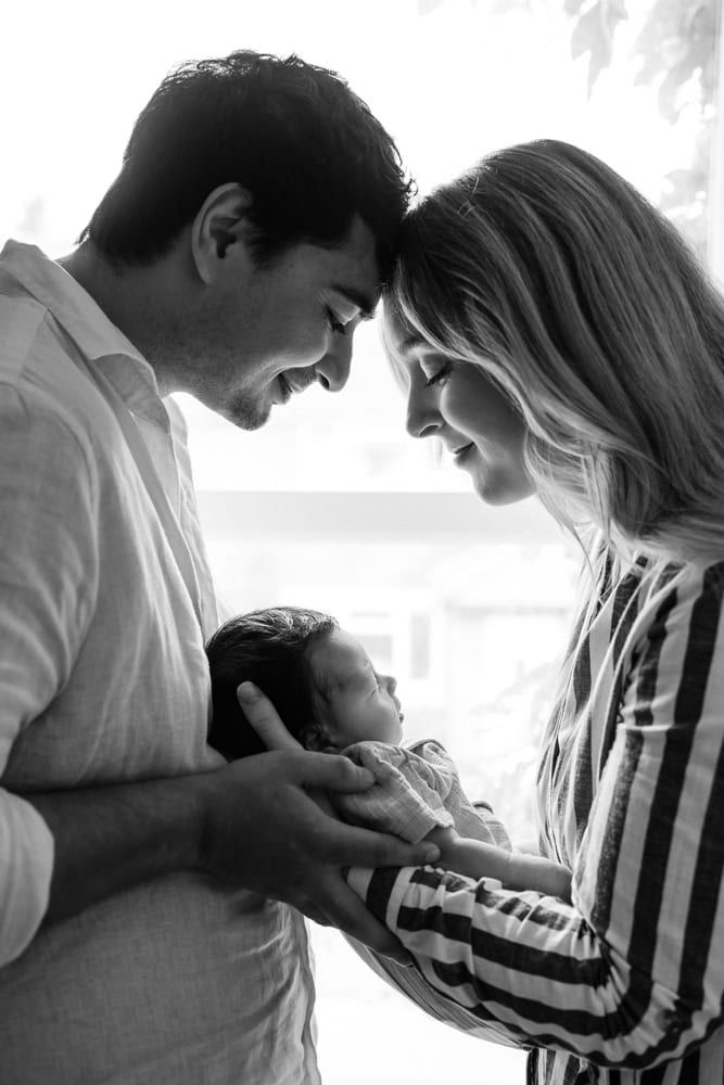 A image of a mother and father facing one another and holding their baby between themselves, taken at an in-home baby shoot in Marlow.