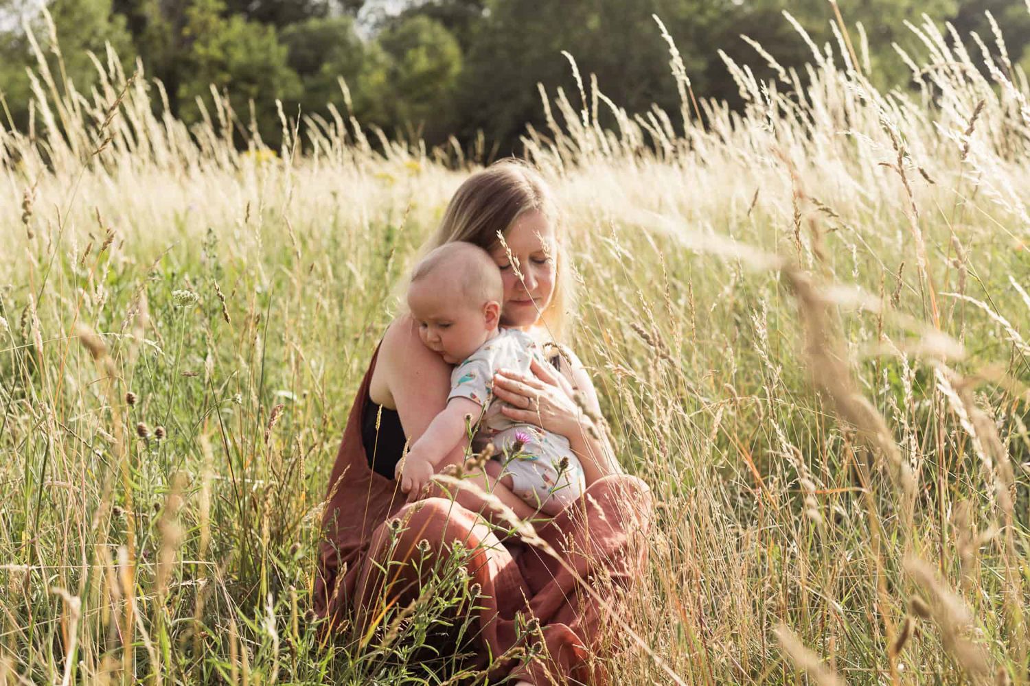 A mother holding her baby in a field of wild flowers.