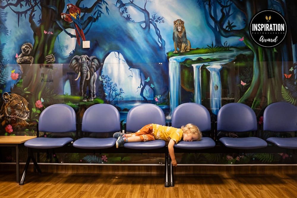 A young boy lies across a row of seats in an a&e waiting room.