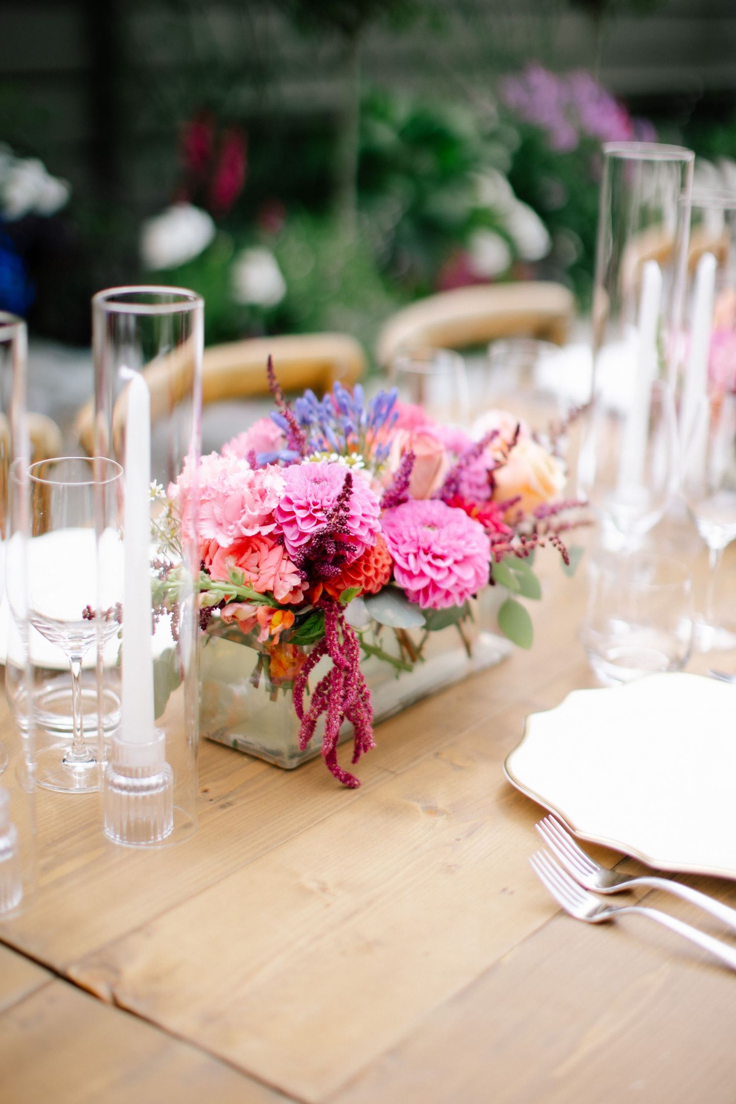 Wedding detail of colourful bouquet and reception styling on wooden table.