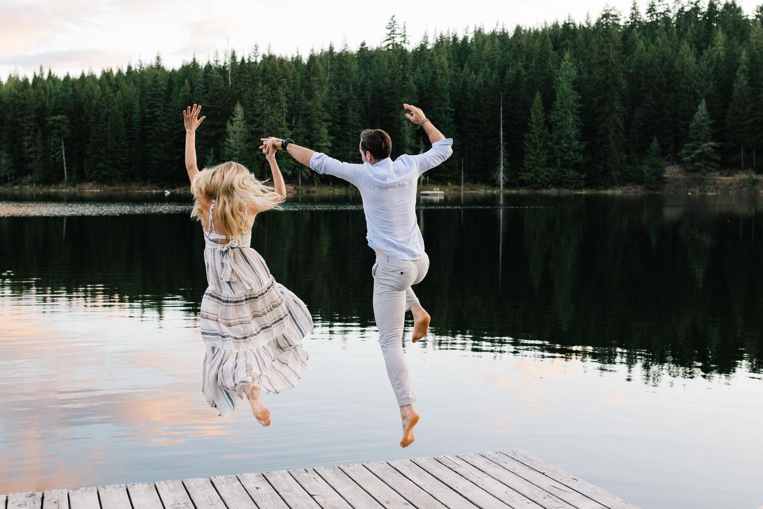 Couple jumping into lake from dock at sunset in Whistler, BC.