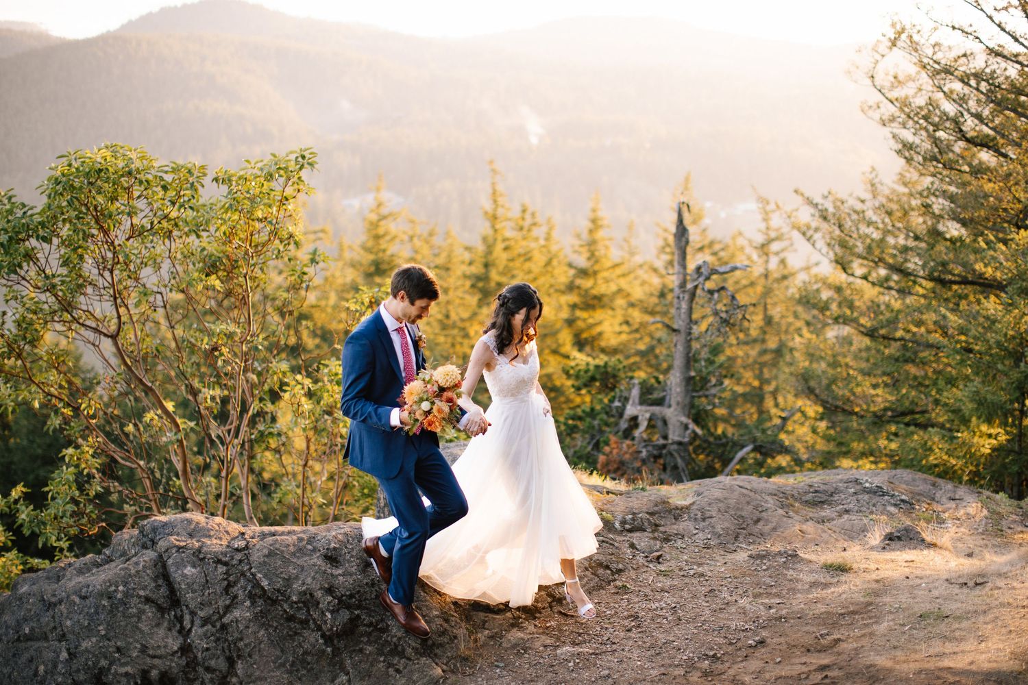 Bride and groom celebrating on a cliff at golden hour above Squamish with forest and valley views.