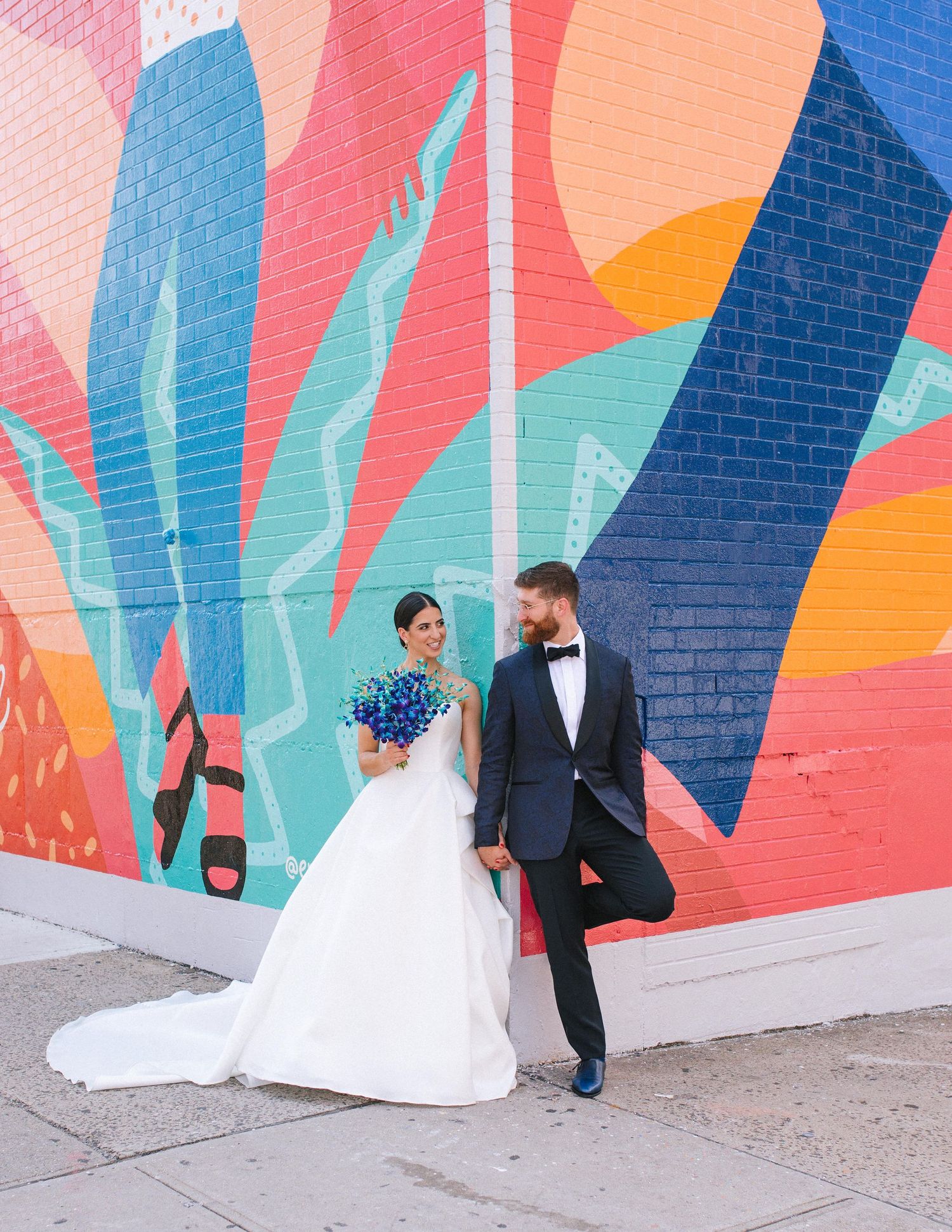 Bride and groom posing in front of colourful mural for modern urban wedding portraits.