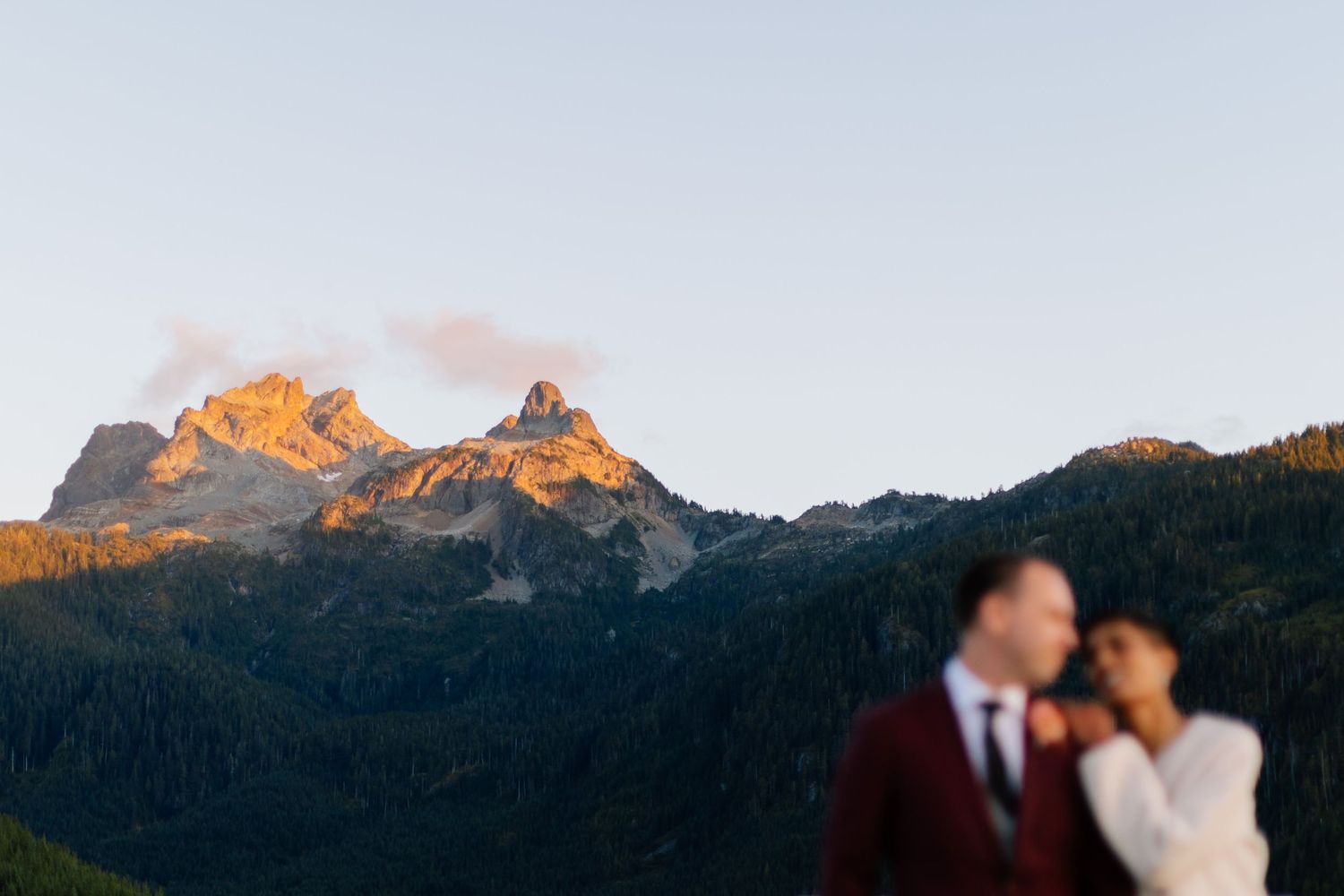 Couple embracing at sunset with glowing alpine peaks behind them in the Squamish mountains.