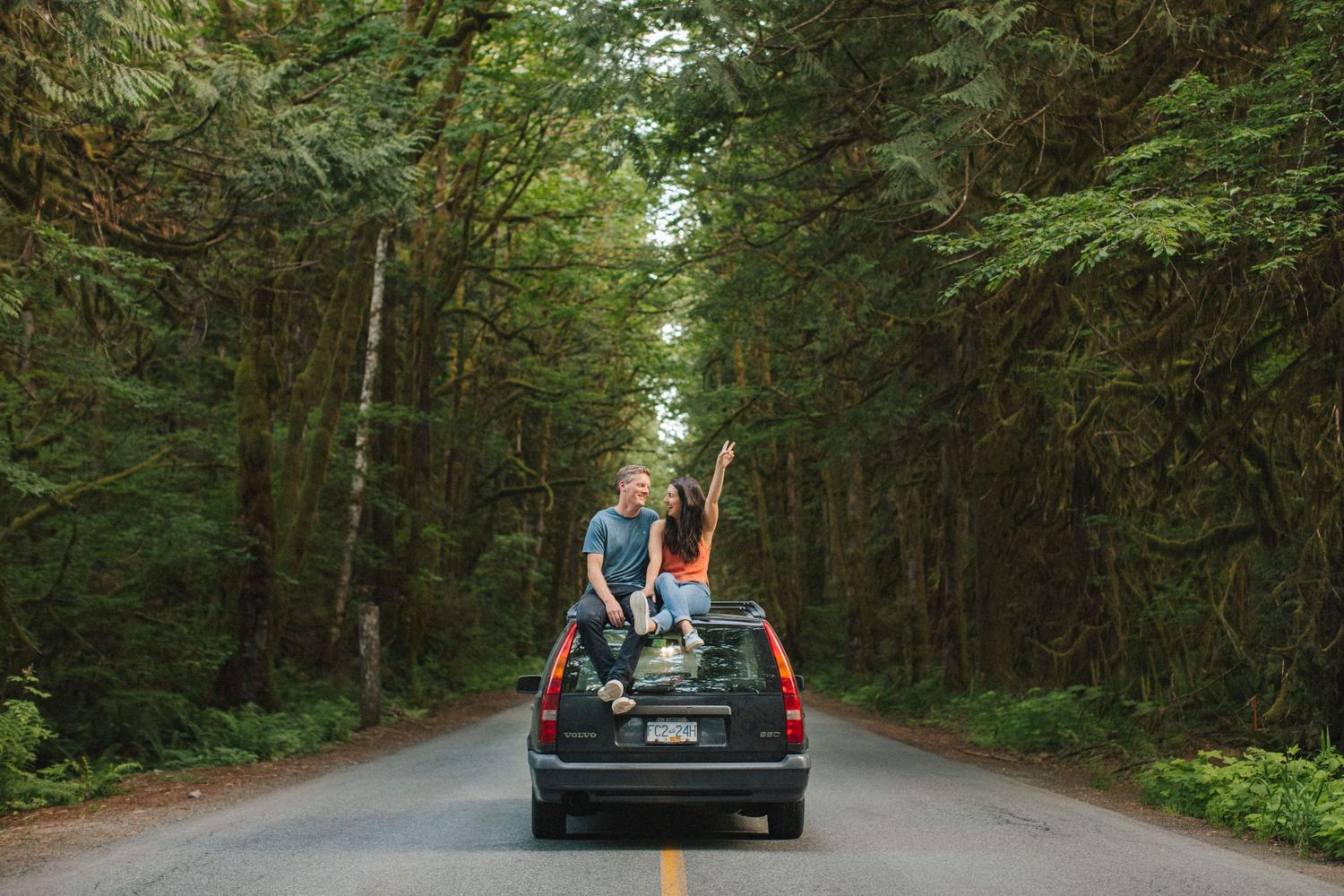 Wedding party celebrating in car driving through forest road.