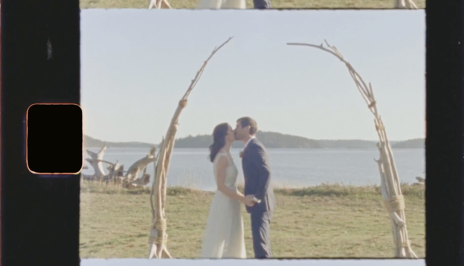 Super 8 wedding film still of couple standing beneath wooden ceremony arch by the ocean.