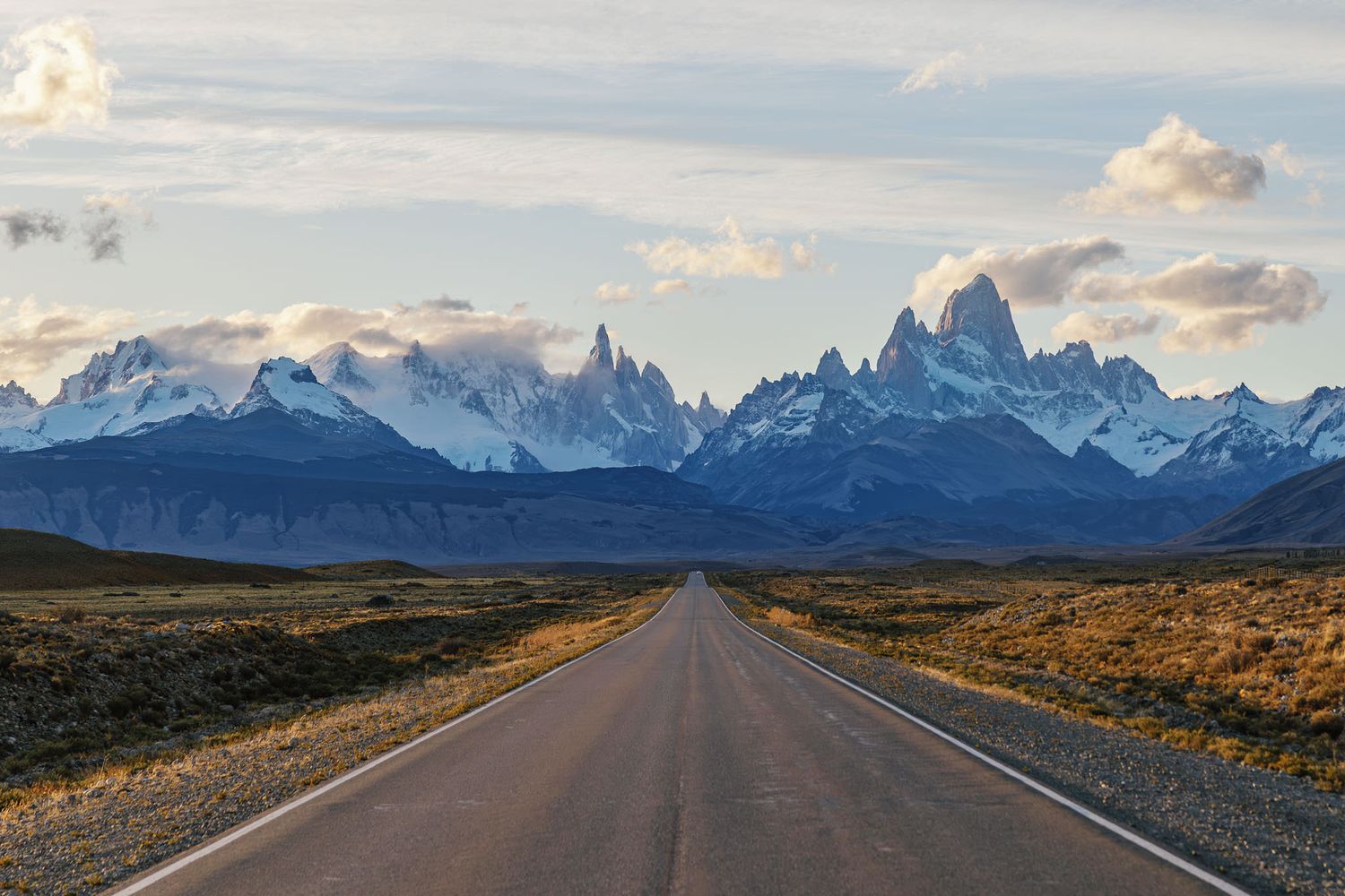 Open road leading toward dramatic mountain range at sunrise.