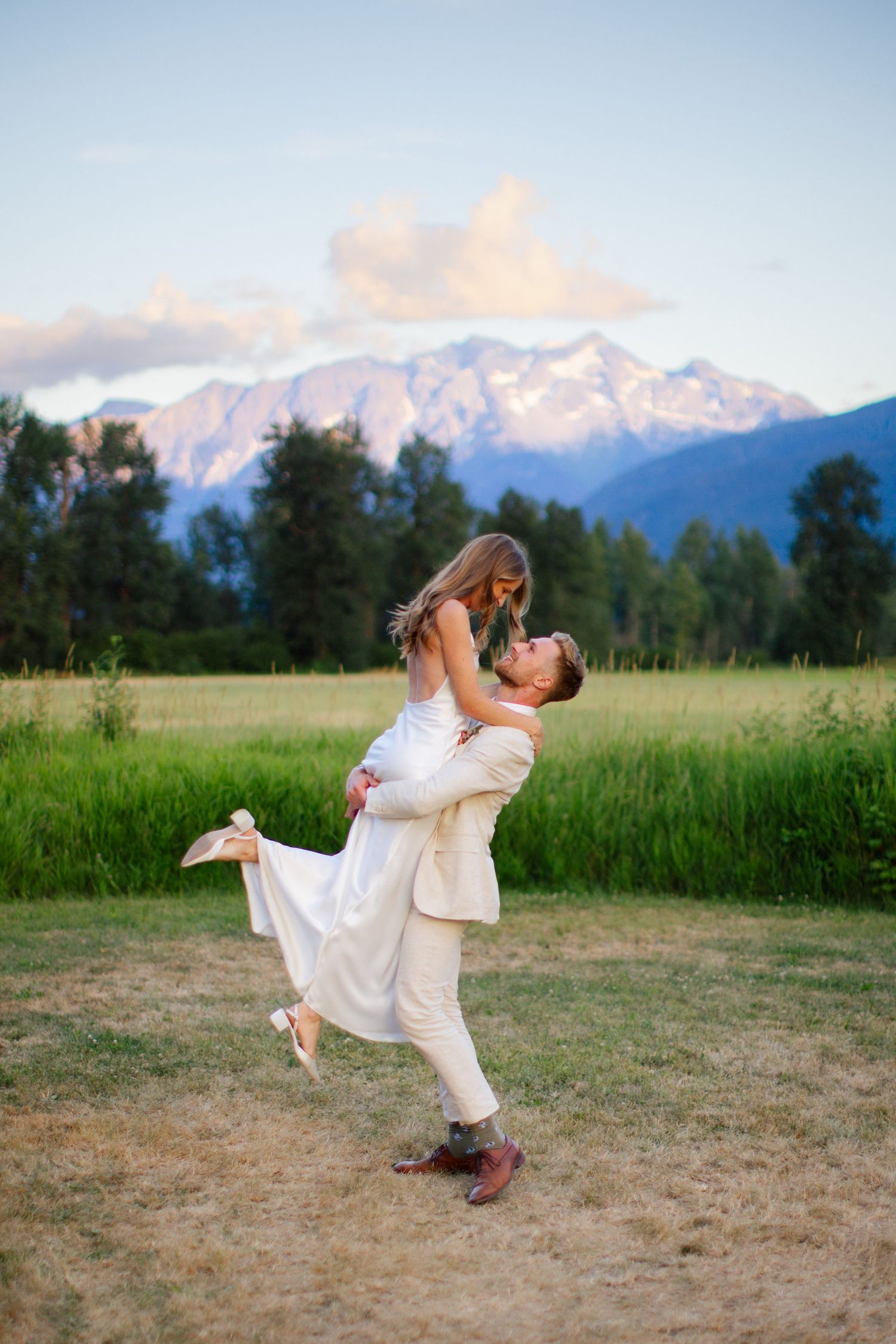 Bride in white dress twirling in a mountain meadow near Squamish with coastal peaks in the background.