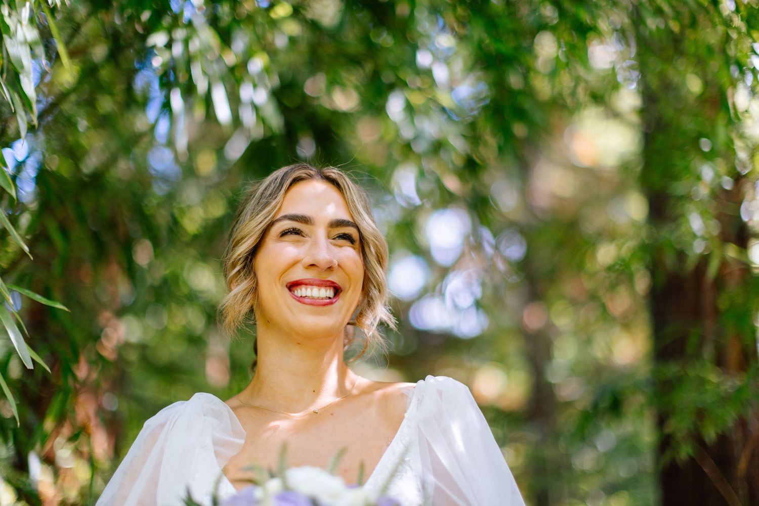Joyful bridal portrait under leafy canopy.