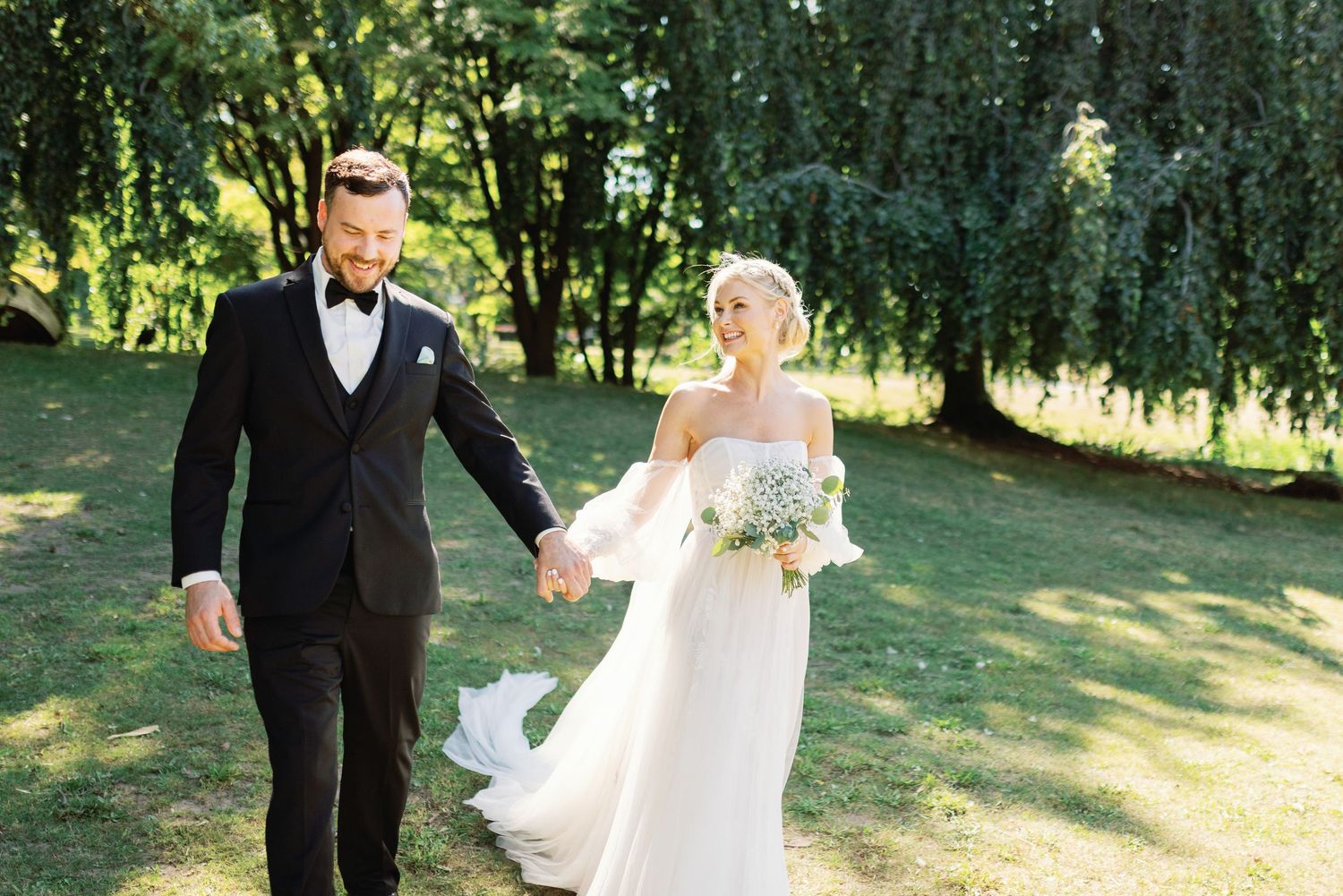 Bride and groom celebrating in sunlit field with mountain views.