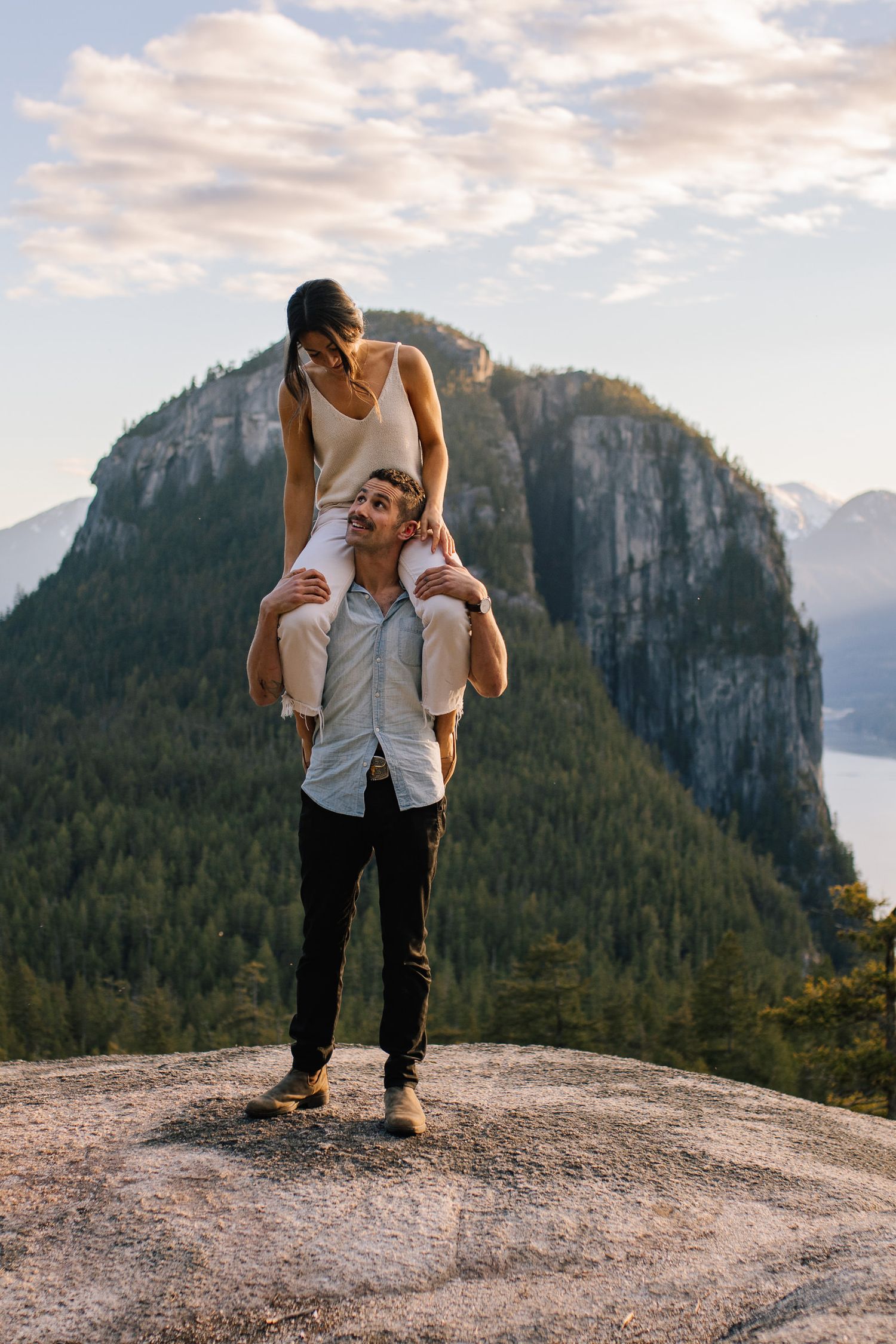 Couple standing on mountain viewpoint in Squamish with dramatic coastal peaks behind them.