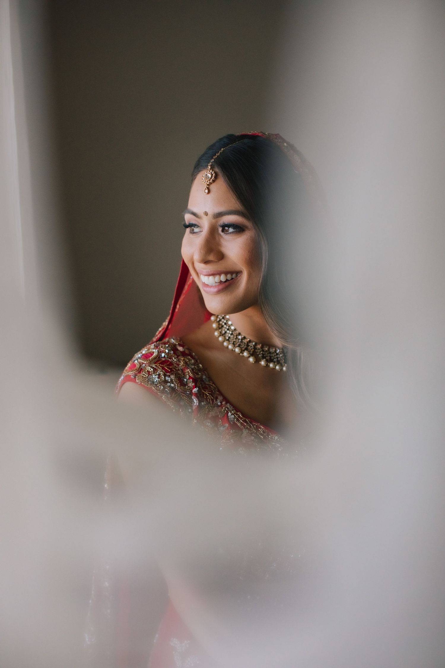 Bride getting ready portrait framed softly through foreground blur.