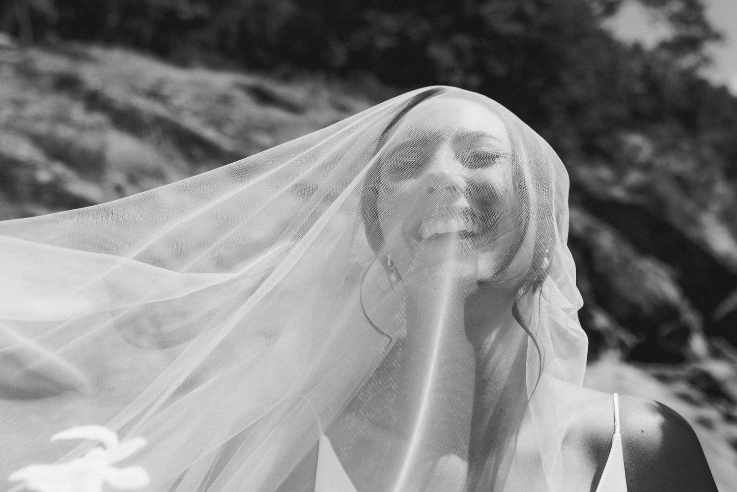 Bride smiling beneath flowing veil in soft light.