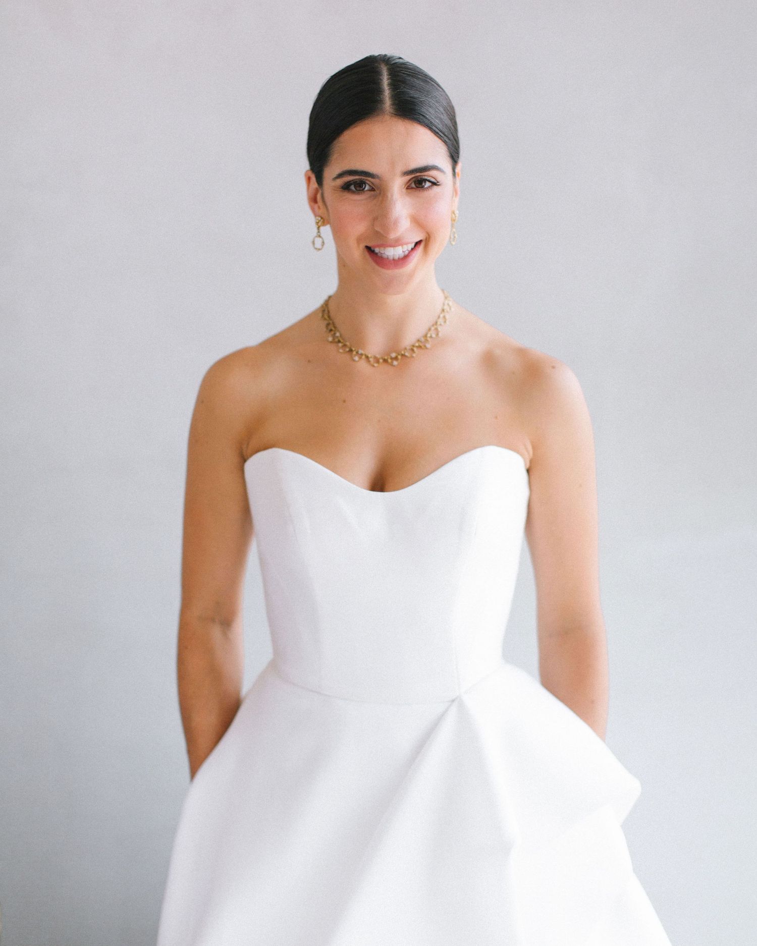 Bride in minimalist white gown against soft studio backdrop.