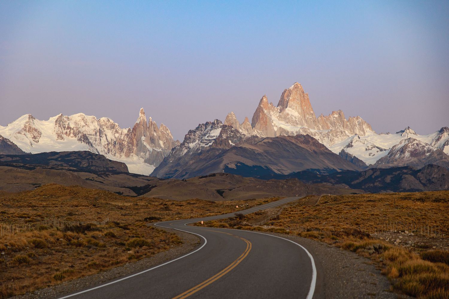 Winding highway leading toward jagged mountain peaks at sunset.