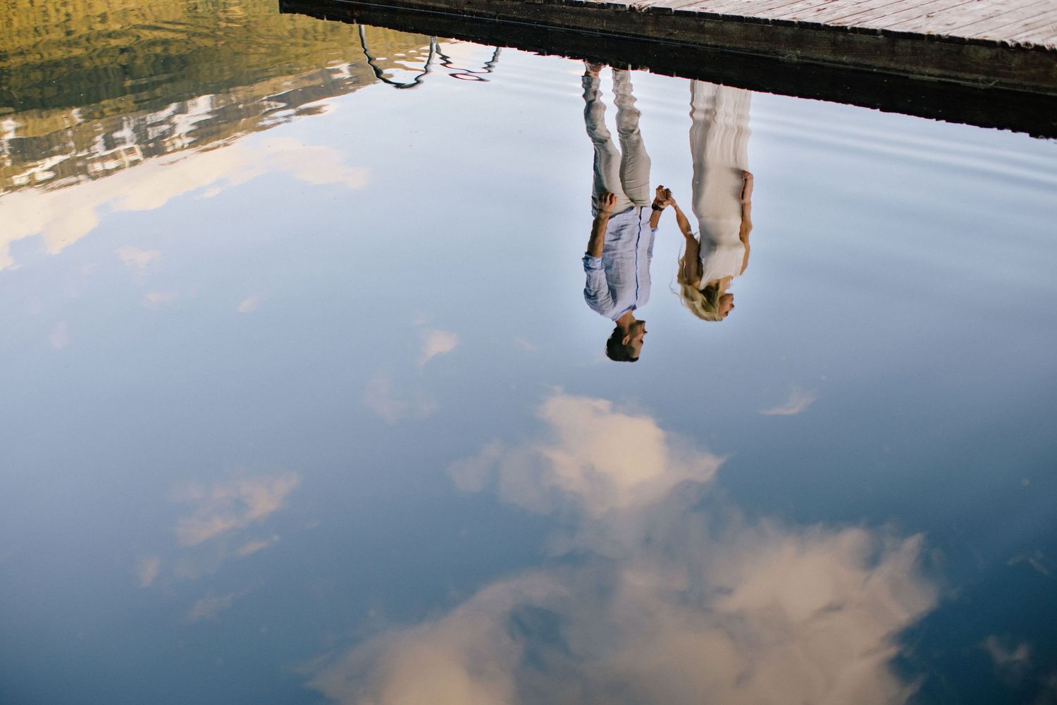 Reflection of couple in calm water at golden hour.