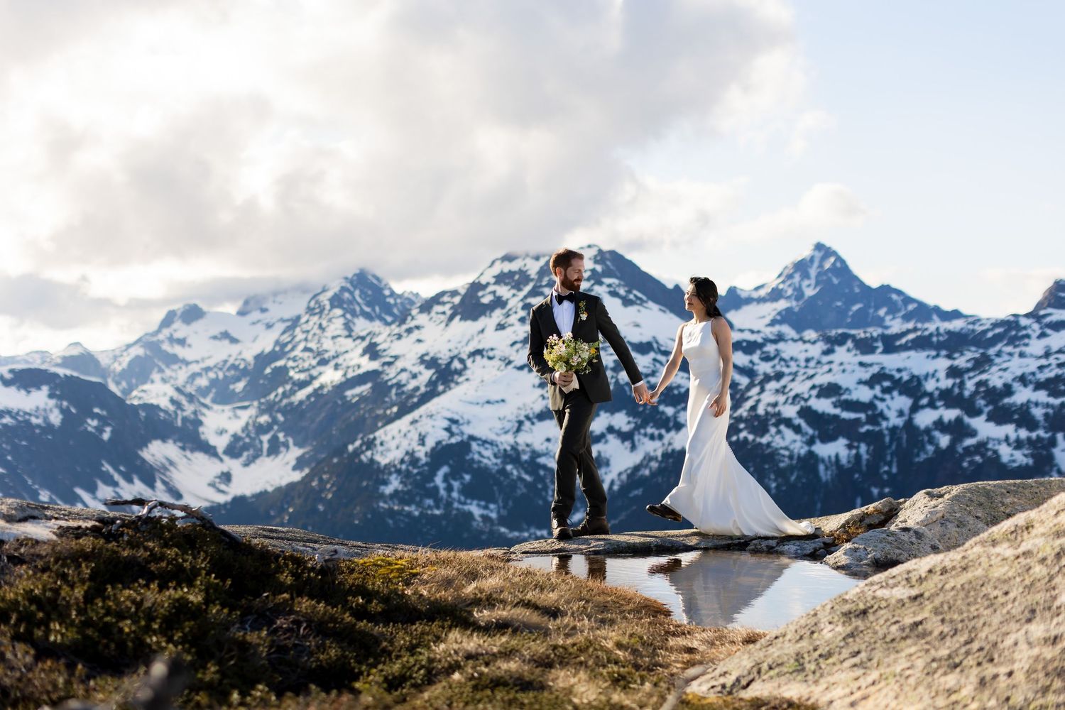 Bride and groom standing on mountain ridge with panoramic views.