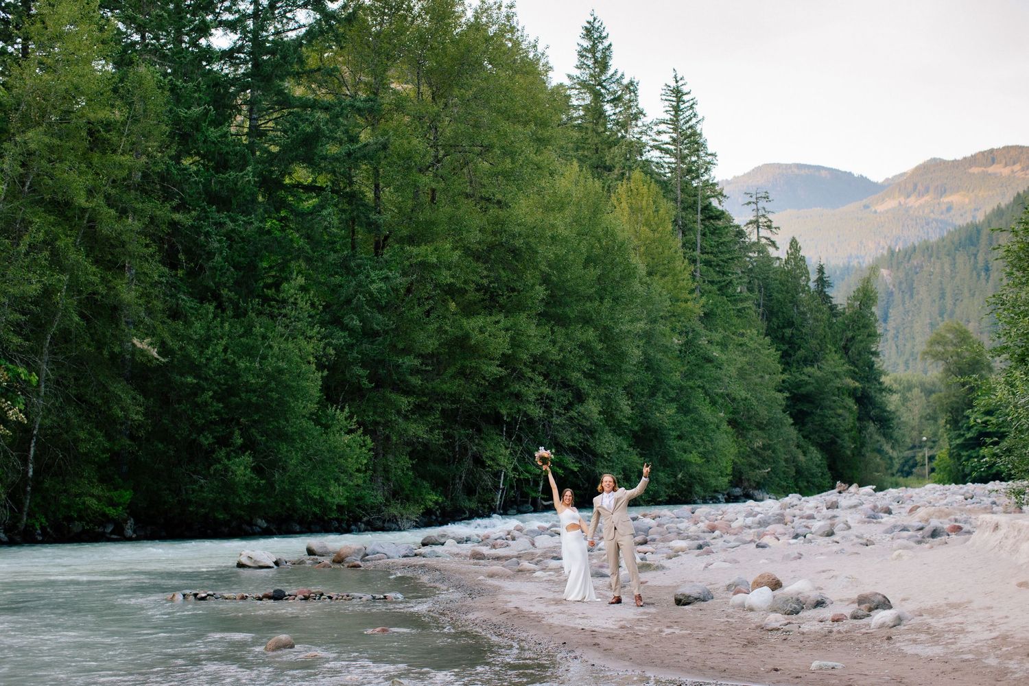 Couple walking along riverbank in forest.