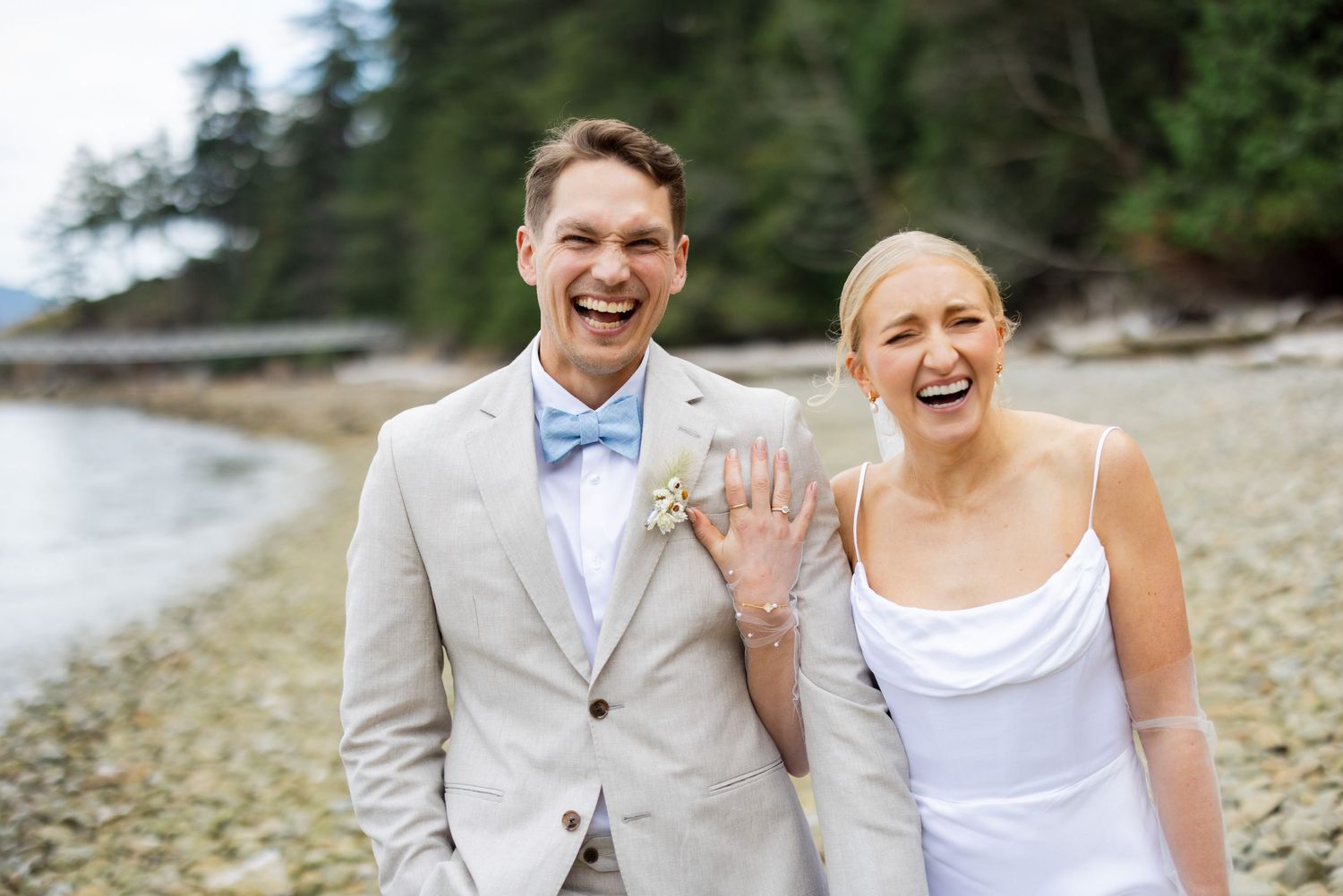 Bride and groom smiling together on rocky beach along the Squamish coastline.