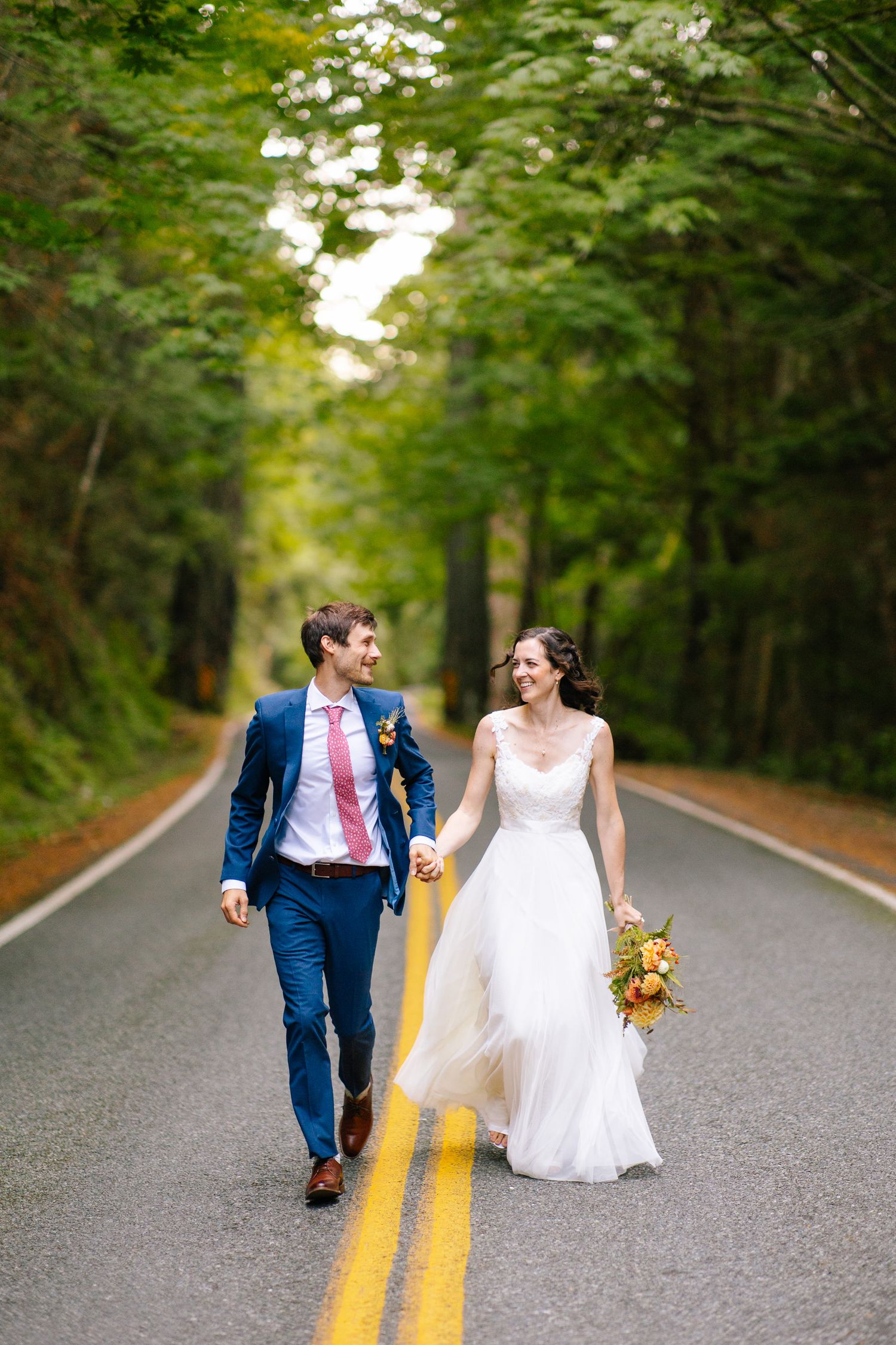 Bride and groom walking hand in hand down a quiet forest road in Squamish.