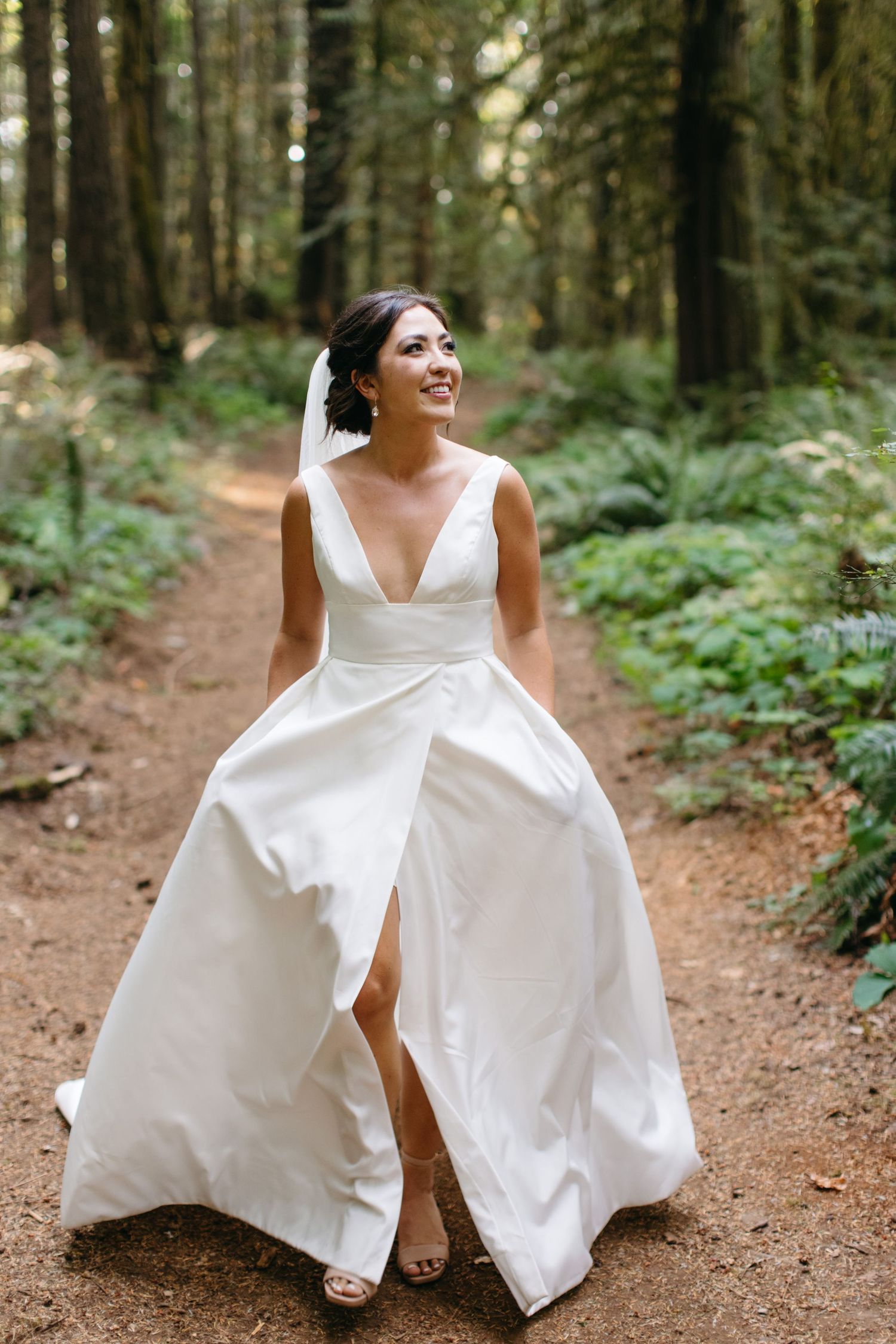 Bride walking through wooded trail in flowing gown.