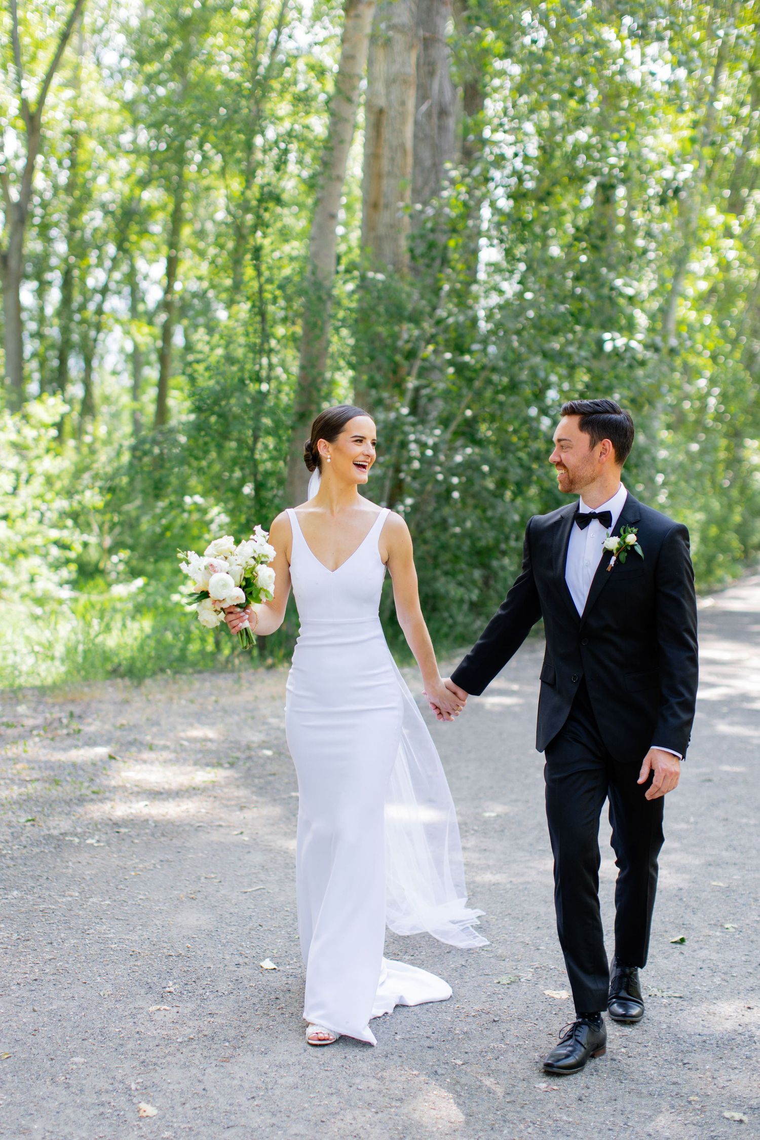 Bride and groom walking hand in hand down forest path.