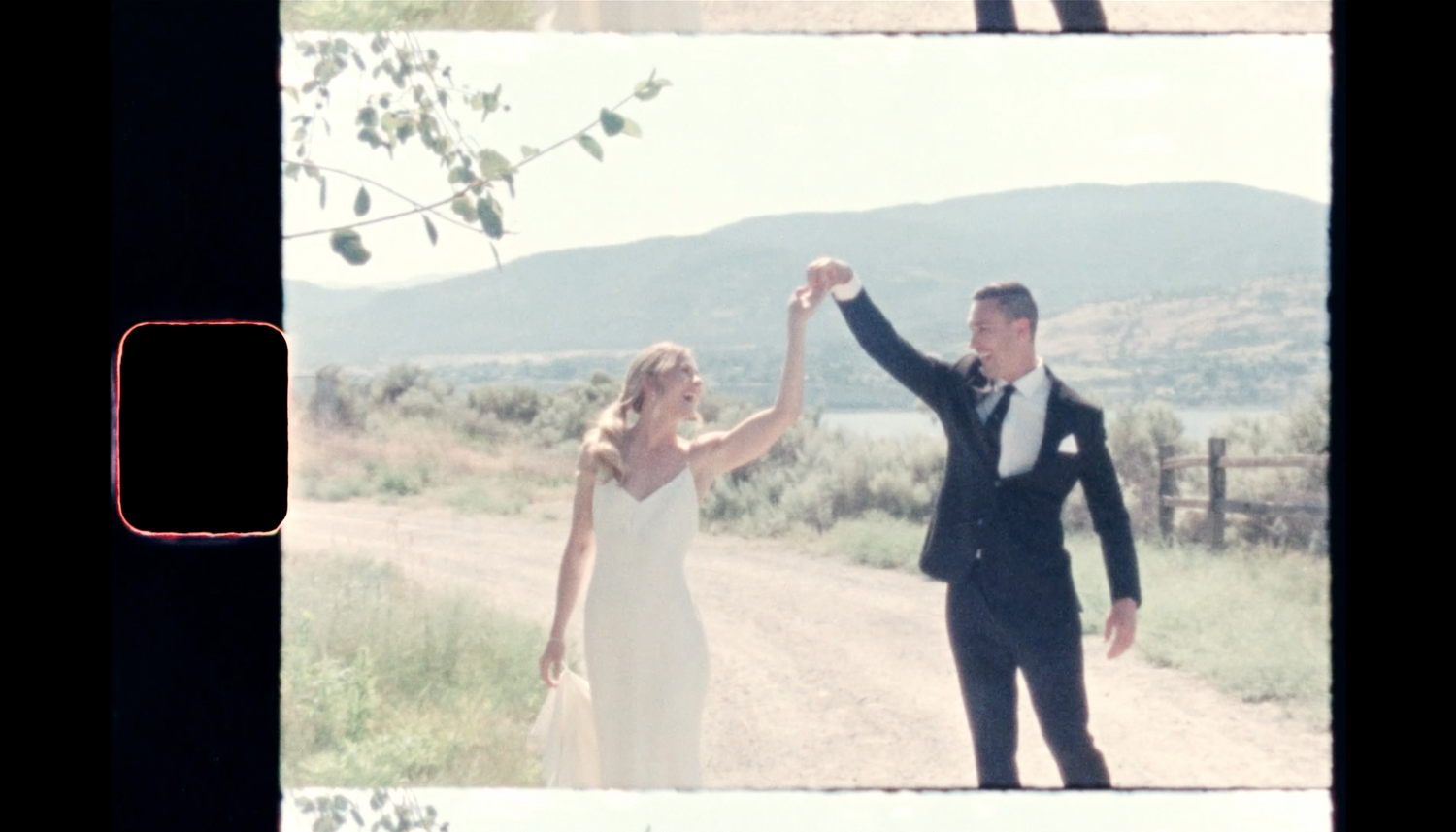Super 8 wedding film frame of bride and groom raising hands in celebration with mountain backdrop.
