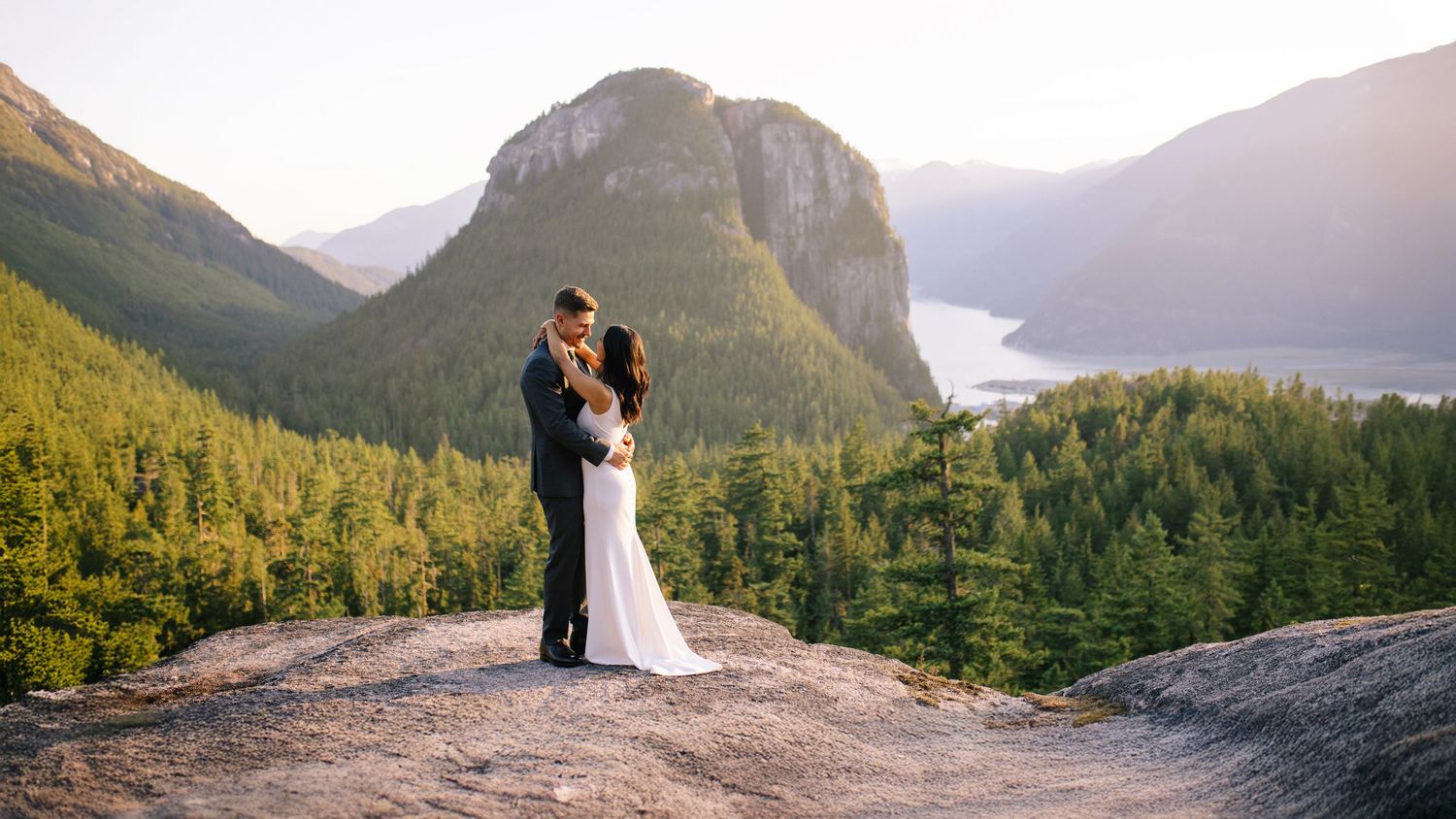 Bride and groom standing on cliffside above Howe Sound in Squamish.