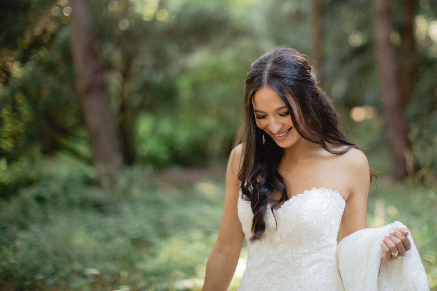 Bride walking through forest in strapless gown.