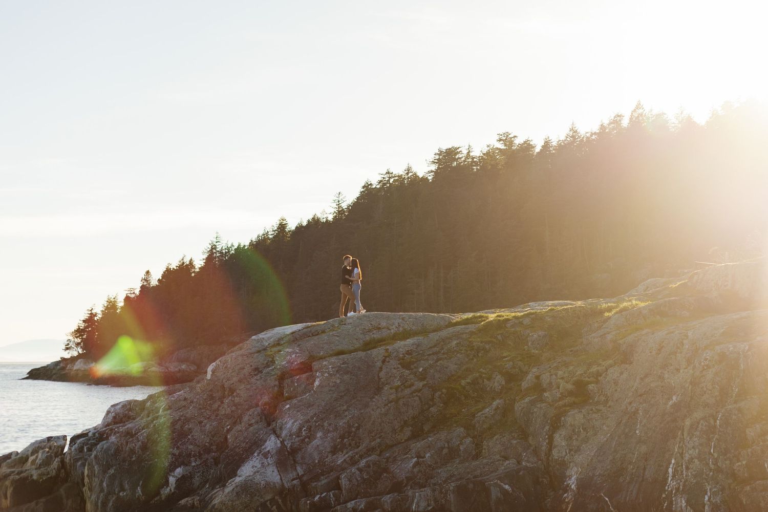 Bride walking along rocky shoreline at sunset.