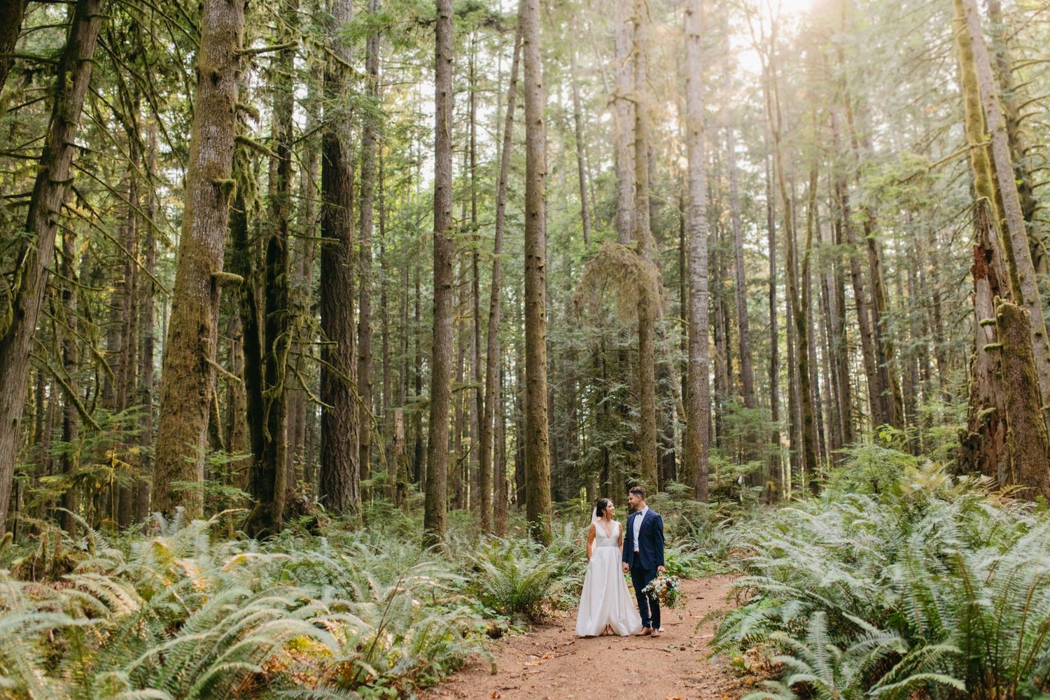 Couple surrounded by towering trees in Pacific Northwest forest.